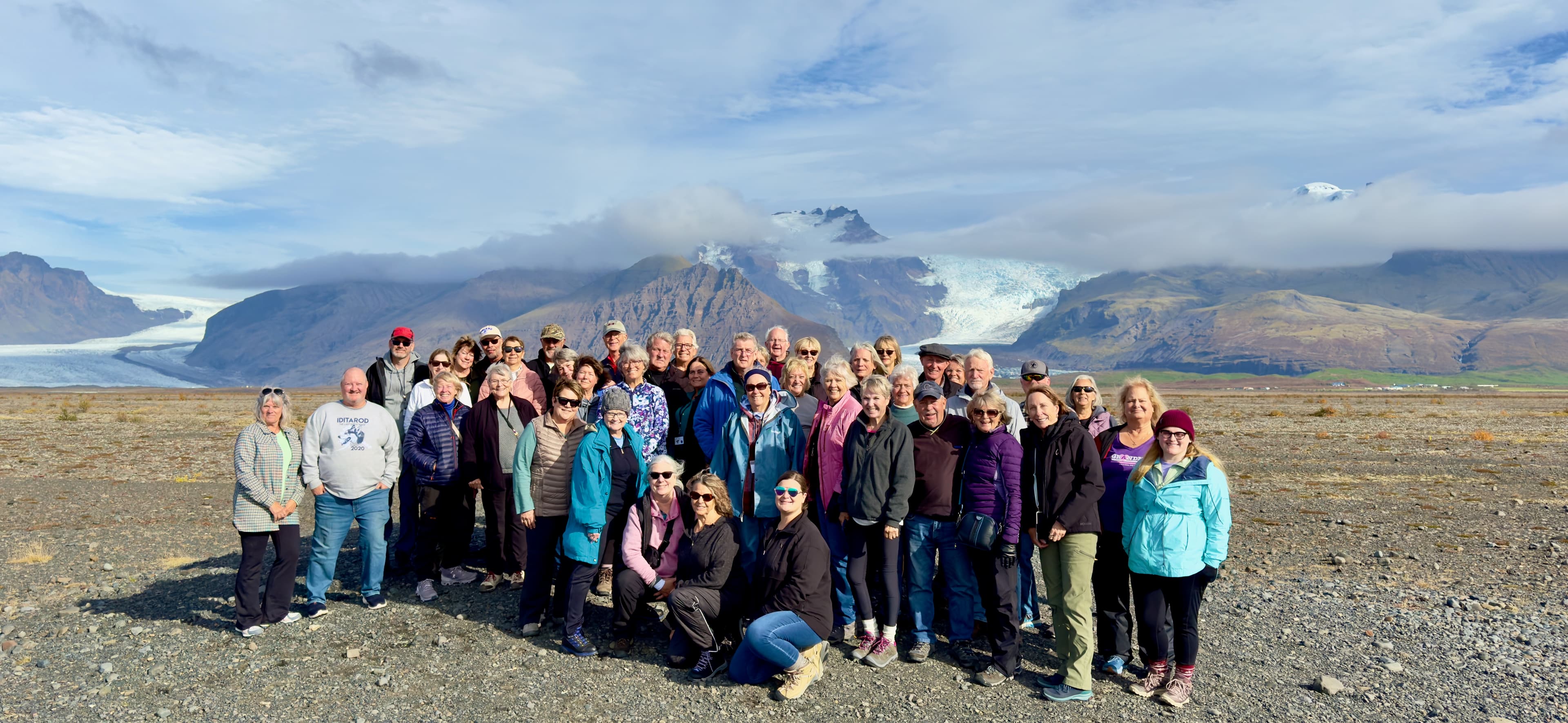 An adult group traveling together in Iceland with mountains and a glacier behind them